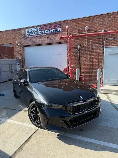 First Choice Collision Center sign above the shop entrance with a black BMW parked outside